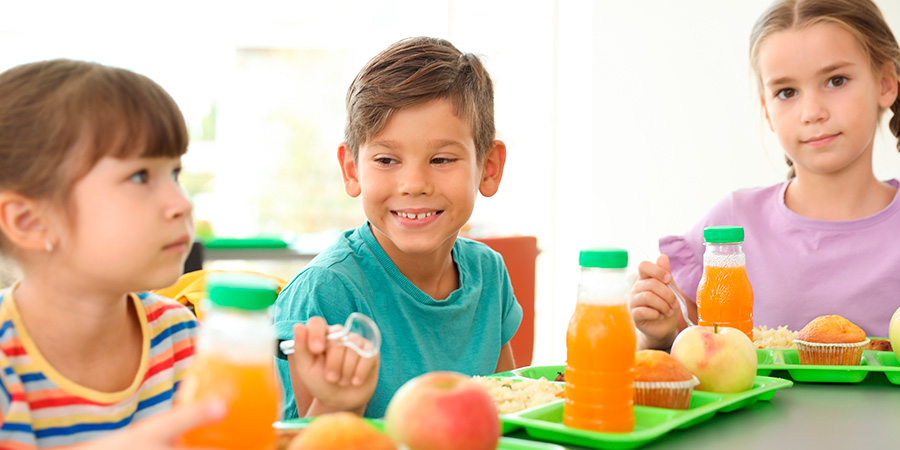 Crianças sentadas à mesa com frutas, sucos e outros alimentos saudáveis sobre as bandejas
